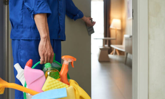 Professional cleaner with bucket of detergents opening room